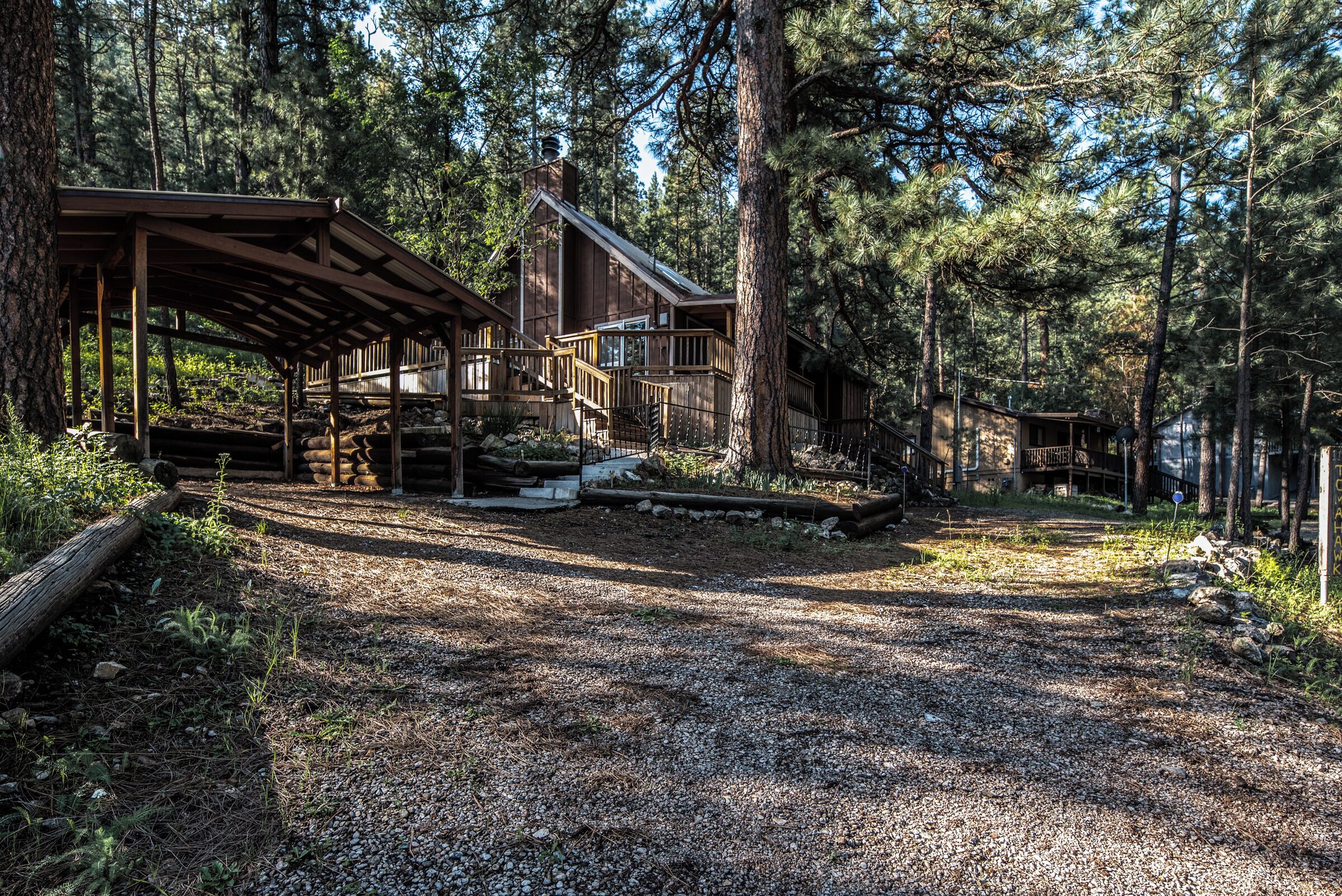 A rustic cabin with a covered porch, a staircase leading to a deck, and a gravel path.
