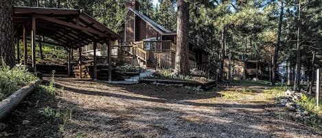 A rustic cabin with a covered porch, a staircase leading to a deck, and a gravel path.