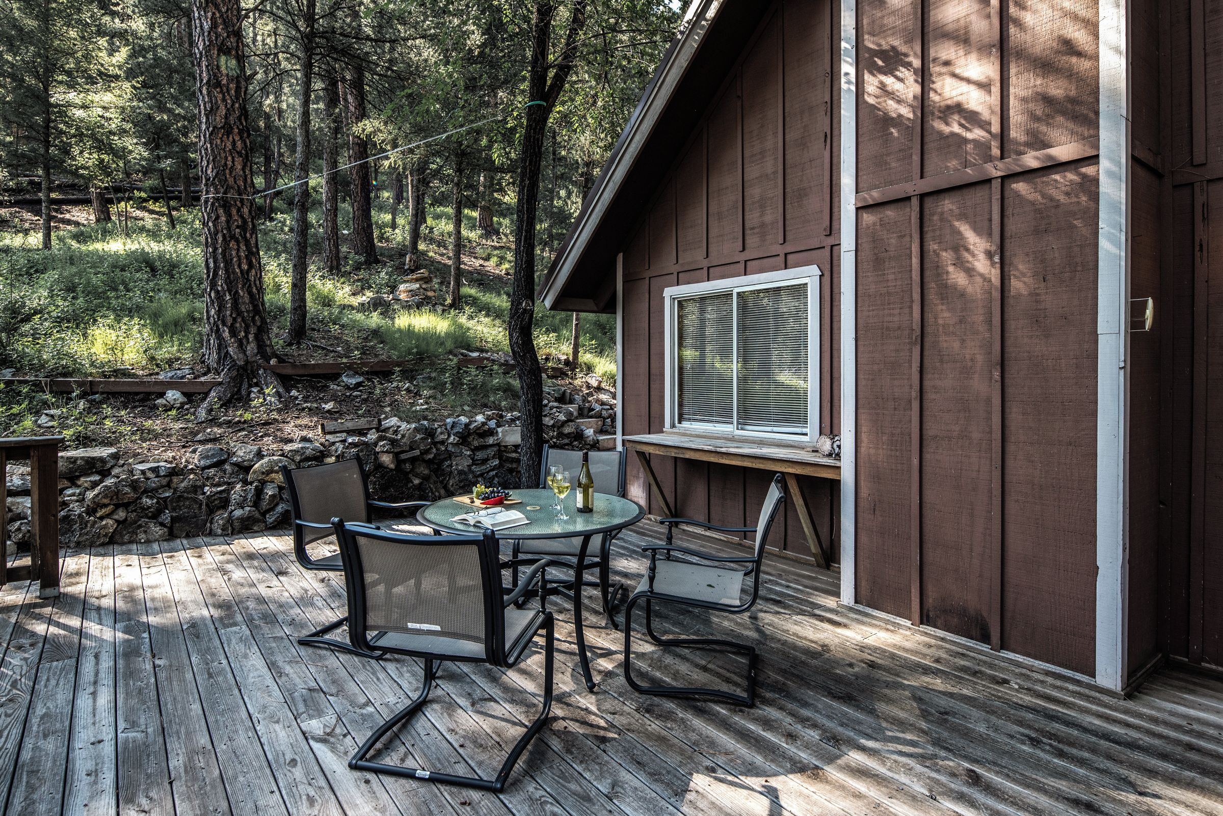 A wooden deck with a table and chairs, a stone wall, and a cabin with a window.