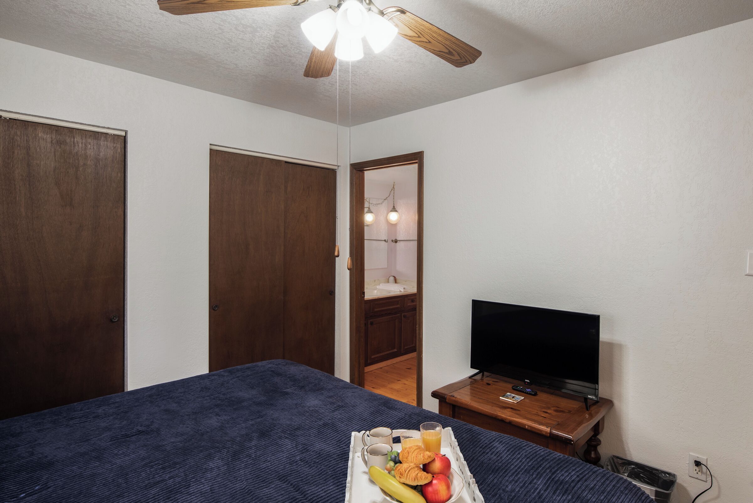 A bedroom with a bed, a television on a wooden table, and a tray with breakfast items.