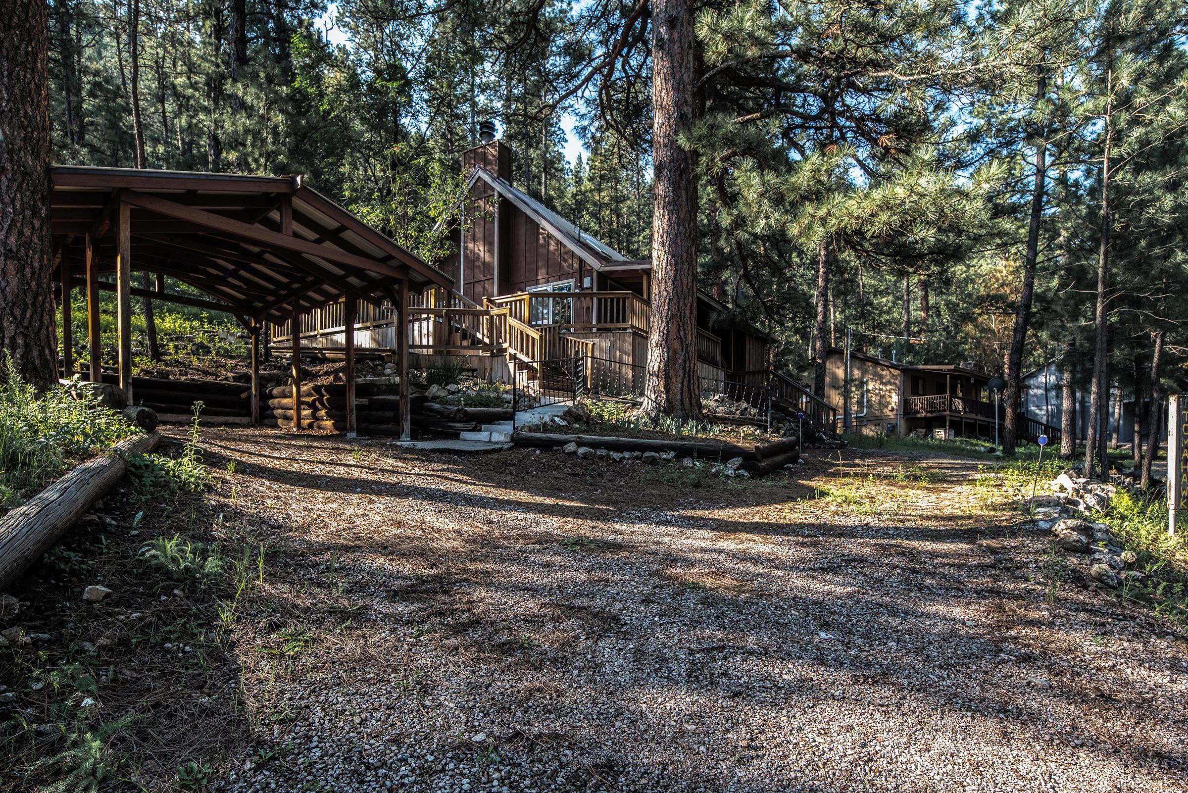 A rustic cabin with a covered porch, a staircase leading to a deck, and a gravel path.