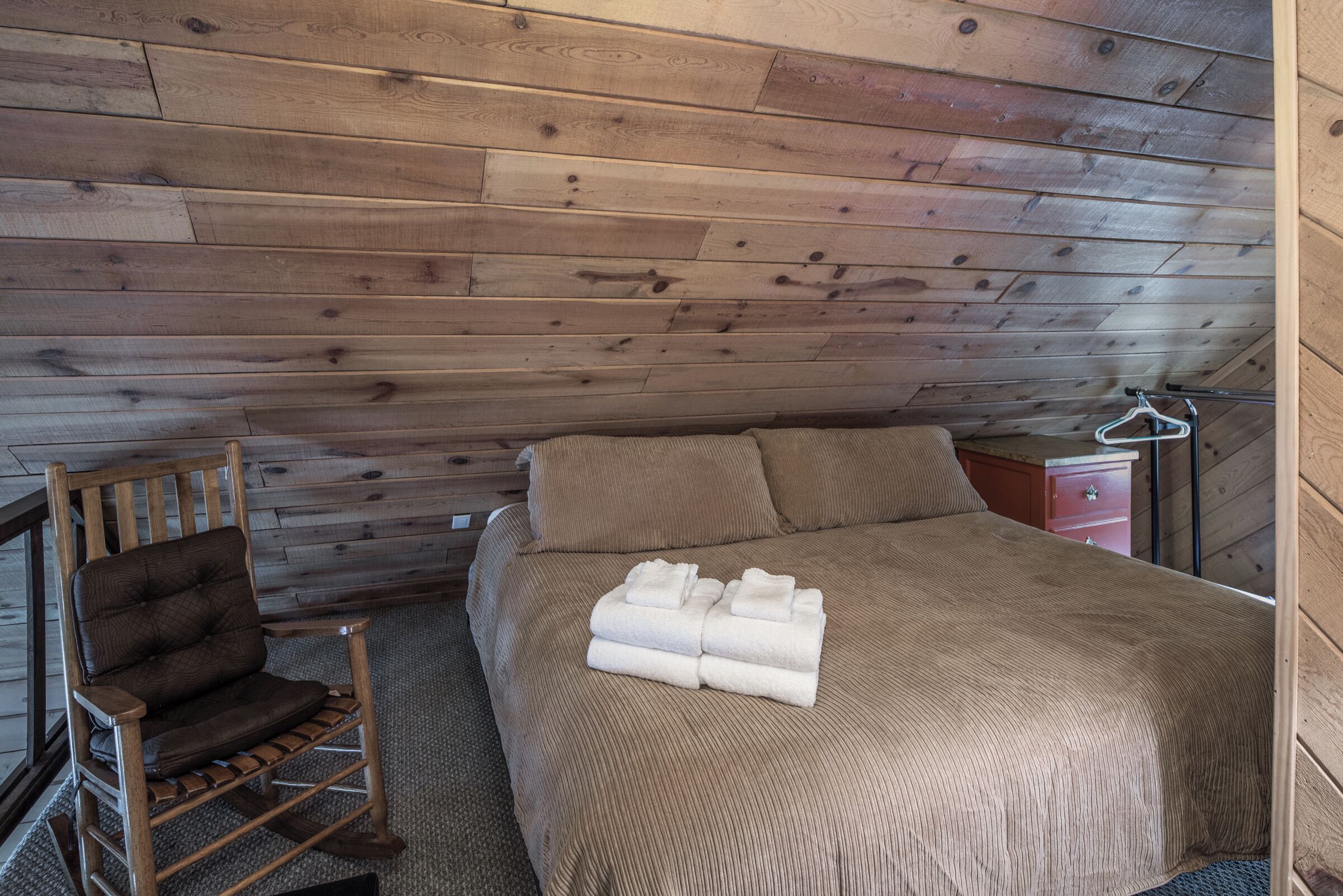 Una habitación con paneles de madera, una cama, una silla y un pequeño aparador.