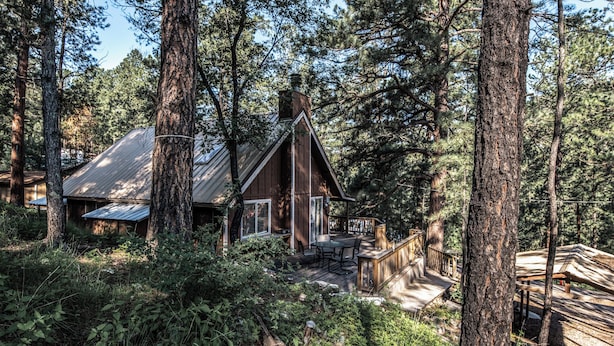 A cabin surrounded by tall trees, with a deck and outdoor seating area. - Rock'inn Pines by Ruidoso Vacation Rentals (Ruidoso)