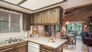 A kitchen with wooden cabinets, a dishwasher, and a dining area with a table and chairs. - Rock'inn Pines by Ruidoso Vacation Rentals (Ruidoso)