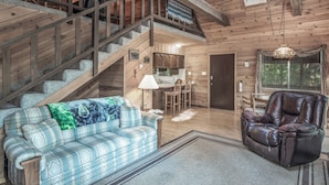 A cozy cabin interior with a wooden staircase, a sofa, a leather recliner, a dining area, and a kitchen. - Rock'inn Pines by Ruidoso Vacation Rentals (Ruidoso)