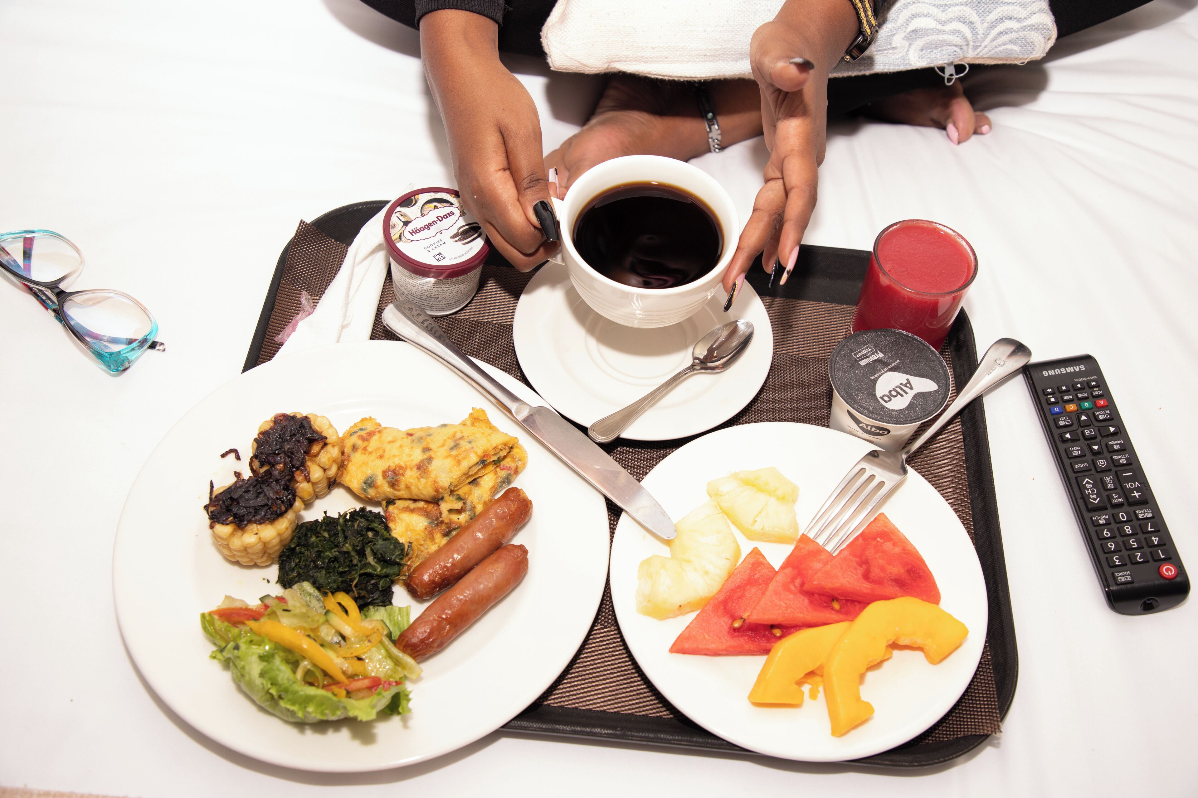 A tray with breakfast items, a cup of coffee, a glass of juice, and a remote control.