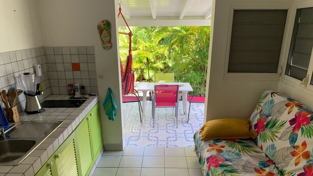 Une cuisine avec un évier, des placards verts et une chaise rouge à l’extérieur.