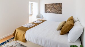 Une chambre à coucher comprenant un lit, une fenêtre, une chaise et une œuvre d’art murale.