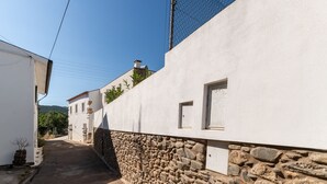 Une rue étroite bordée de bâtiments blancs et de murs en pierre, sous un ciel dégagé.