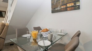 Uma área de refeições com mesa de vidro, cadeiras e uma preparação para café da manhã, incluindo croissants, suco de laranja e xícaras de café.
