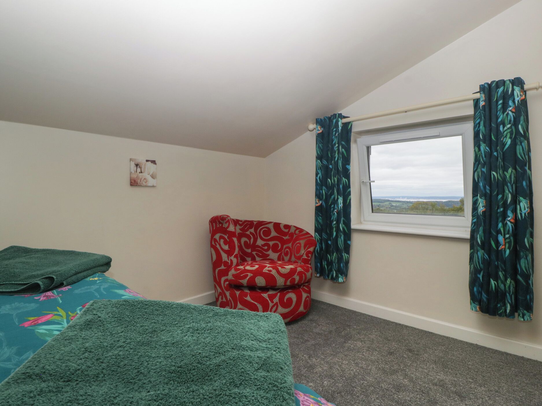 Un dormitorio con una cama individual, una silla roja con estampado, una ventana con cortinas y un pequeño cuadro en la pared.
