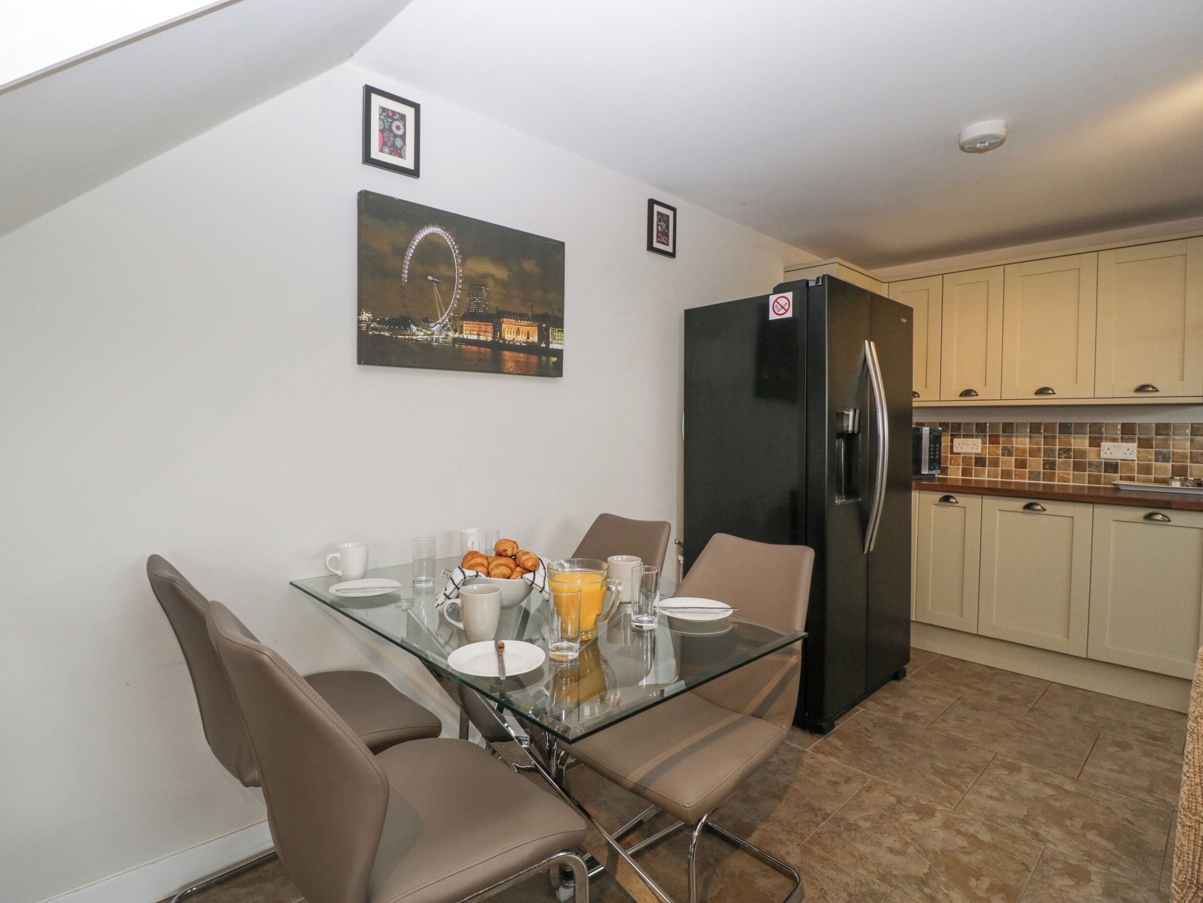 A dining area with a glass table, chairs, and a black refrigerator.