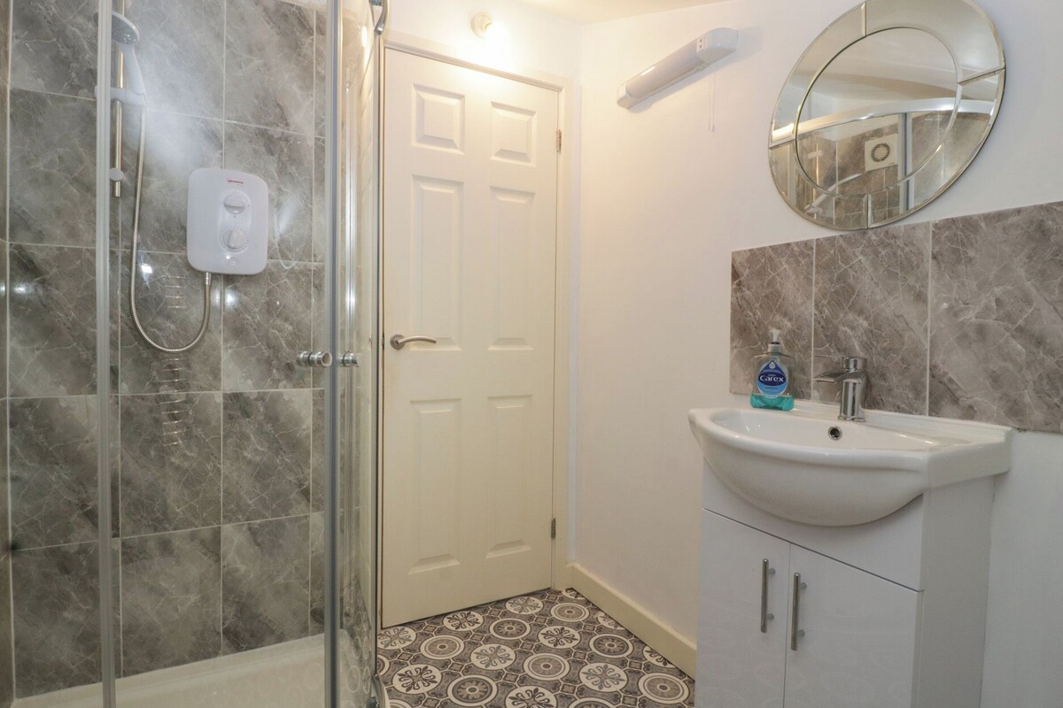 A bathroom with a glass-enclosed shower, a white sink with a mirror above it, and patterned floor tiles.
