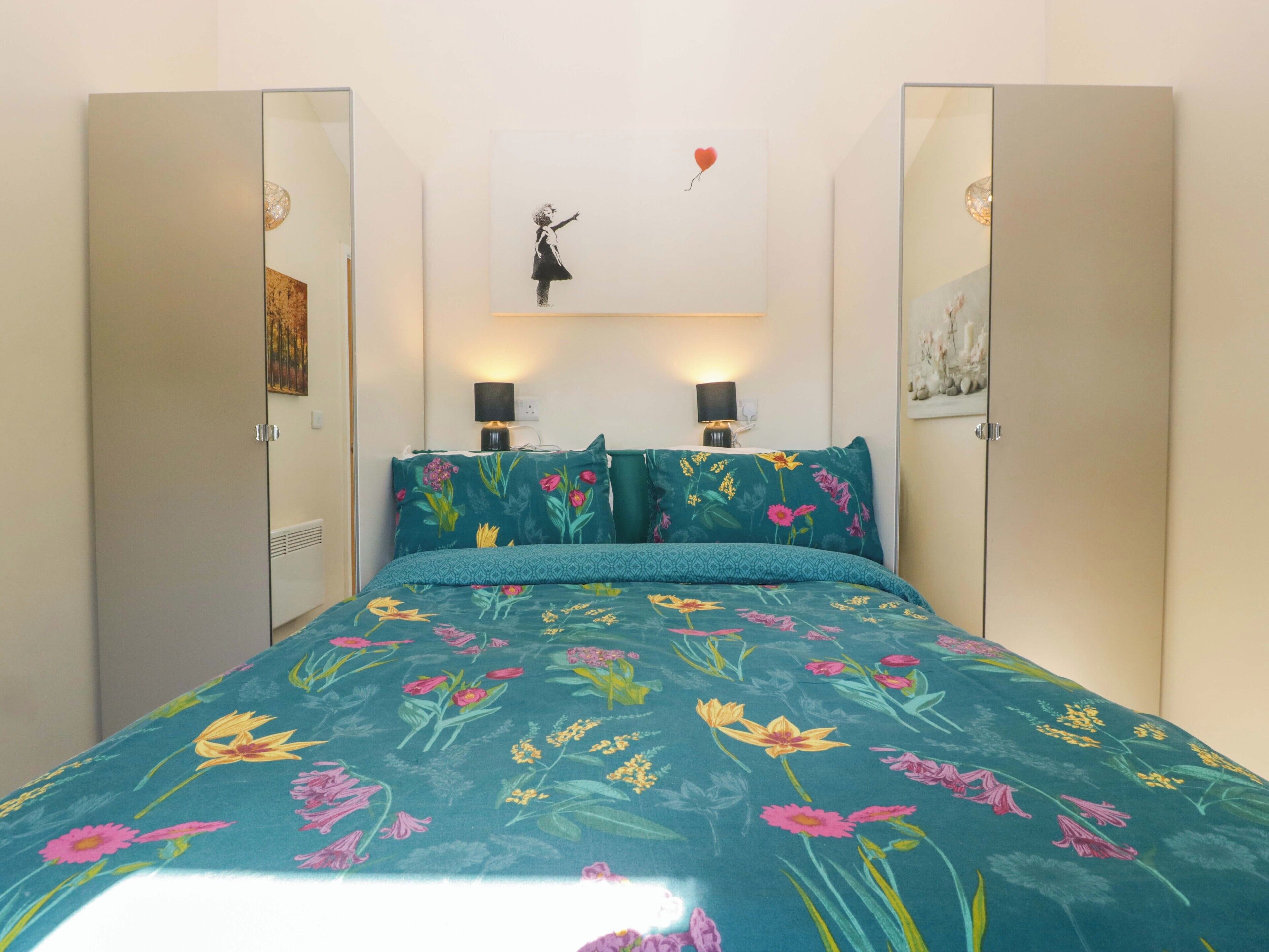 A bedroom with a floral bedspread, two bedside lamps, and a wall-mounted light fixture.