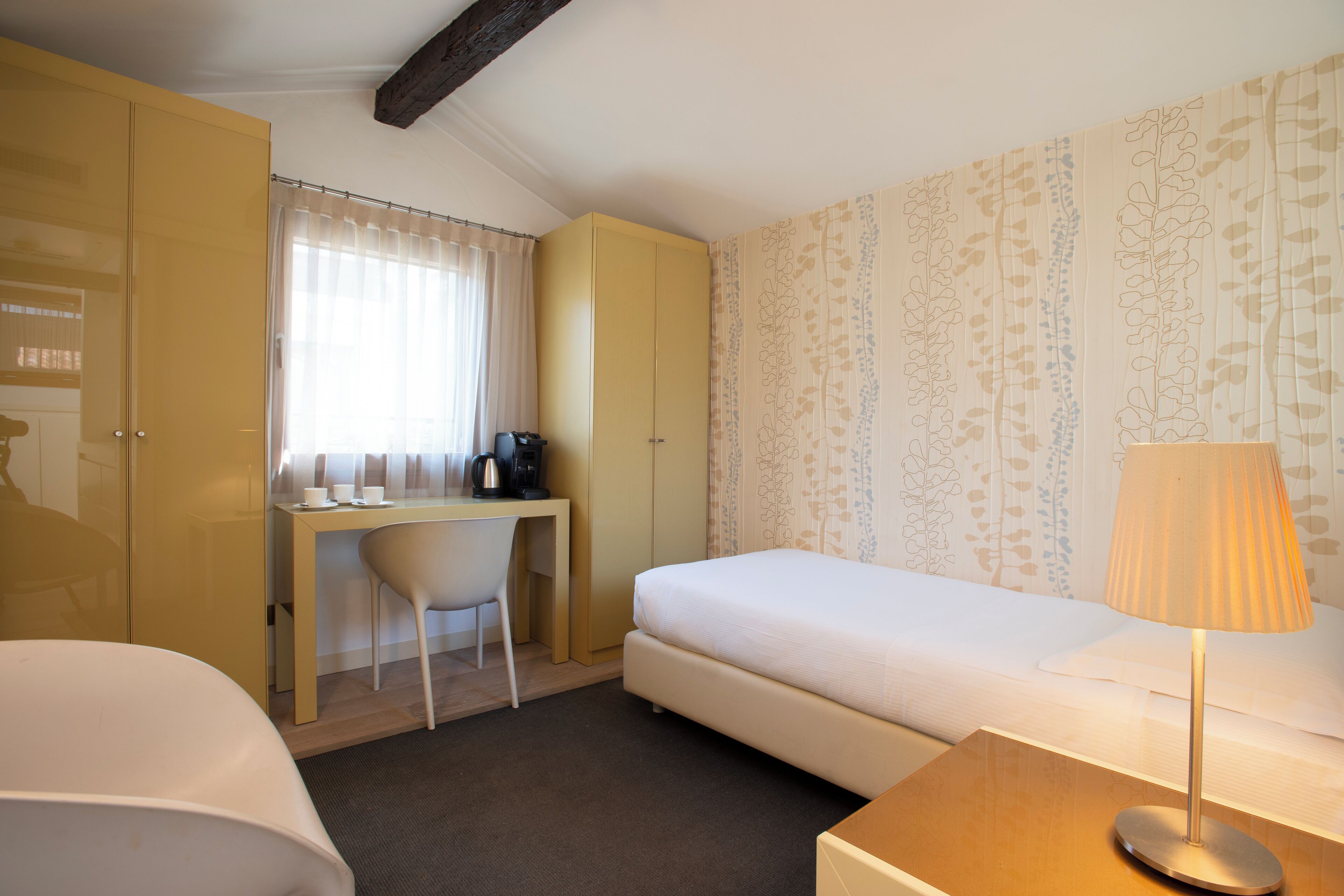 Una habitación de hotel con una cama, un escritorio con una silla, un armario y una lámpara.