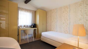 Una habitación de hotel con una cama, un escritorio con una silla, un armario y una lámpara.