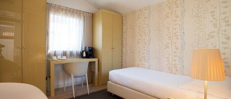 Una habitación de hotel con una cama, un escritorio con una silla, un armario y una lámpara.
