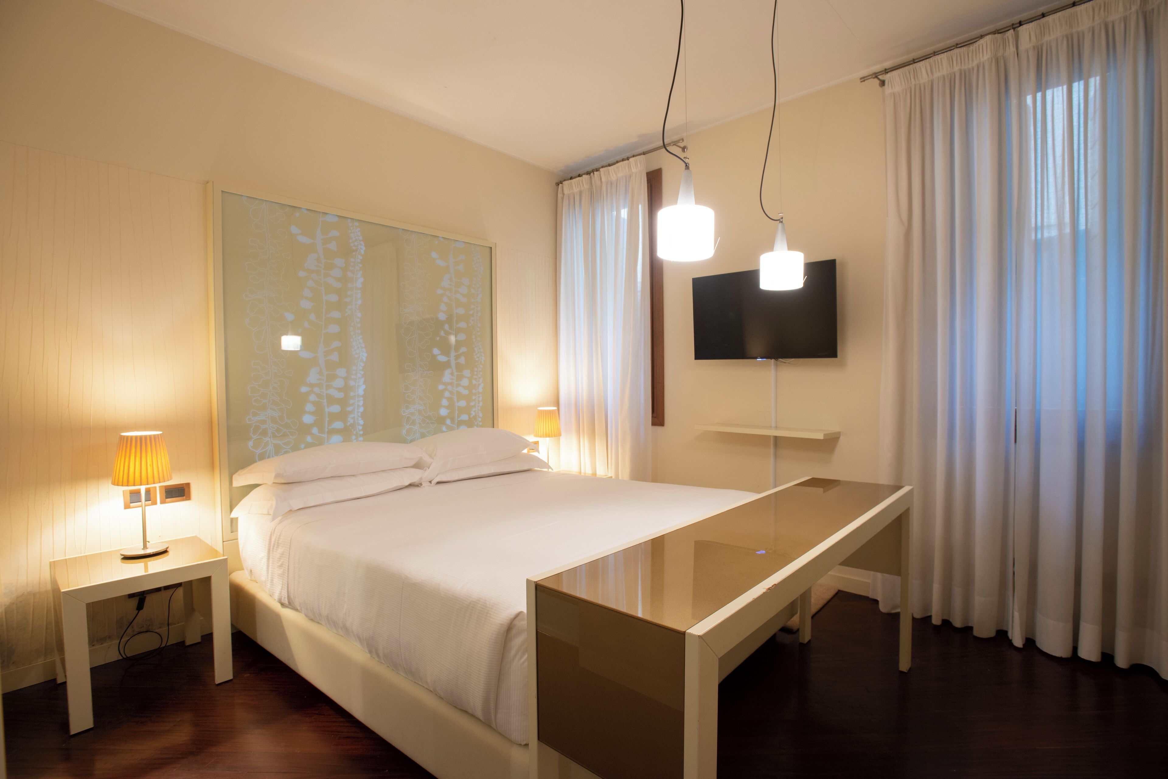 Una habitación de hotel con cama, mesita de noche, lámpara, televisor y cortinas.