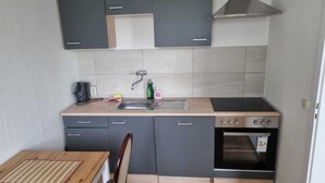 Une cuisine de taille réduite avec des meubles gris, un plan de travail en bois, un évier, une cuisinière et une chaise.