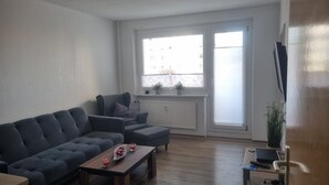 Un salon moderne avec un canapé gris, une table basse en bois et un petit téléviseur posé sur un meuble.