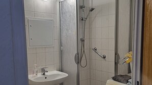 Une salle de bain compacte comprenant une douche, un lavabo et un lave-linge.