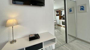 Ein modernes Wohnzimmer mit einem an der Wand befestigten Flachbildfernseher, einer Lampe auf einem Beistelltisch und einer Schiebetür zu einem Küchenbereich.
