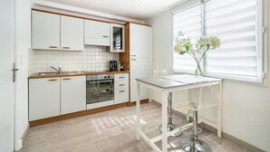 Eine moderne Küche mit weißen Schränken, einem Einbauofen und einem Fenster mit Jalousien.