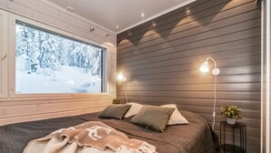 A cozy bedroom with a large window, wooden walls, a bed with pillows, and bedside lamps. - Rukan rinnemaa a by Interhome (Kuusamo)