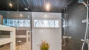 A modern bathroom with a glass shower enclosure, a potted plant, and a view of snowy trees through the window. - Rukan rinnemaa a by Interhome (Kuusamo)