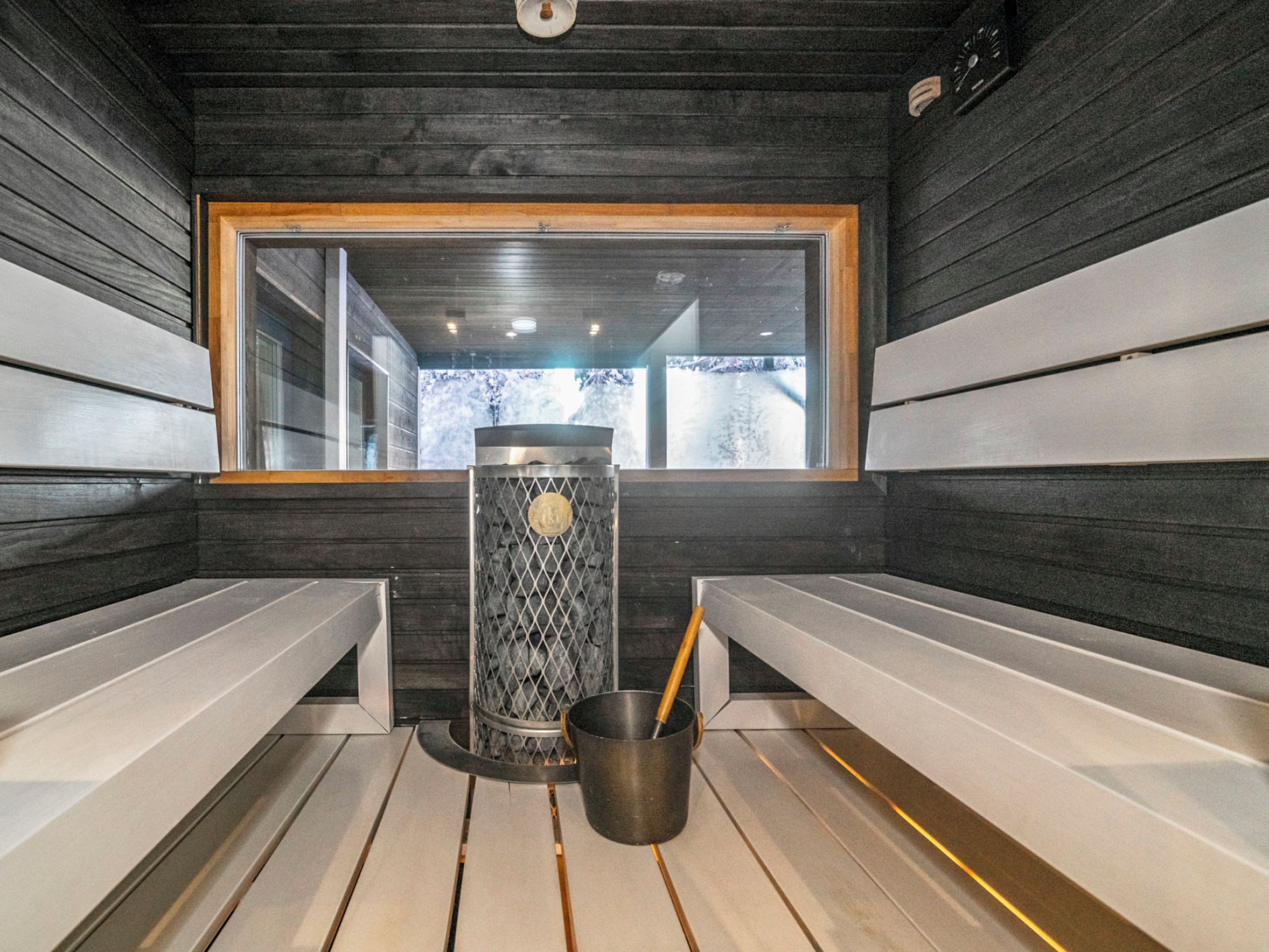 Uma sala de sauna com bancos, aquecedor e janela com vista para o exterior.