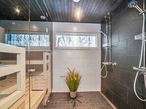 A modern bathroom with a glass shower enclosure, a small window, and a potted plant.