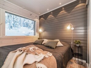 A modern bedroom with a large window, a bed with multiple pillows, a bedside table with a lamp, and a small plant.
