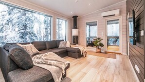 A modern living room with a sectional sofa, a fireplace, and large windows offering a view of snow-covered trees. - Rukan rinnemaa a by Interhome (Kuusamo)