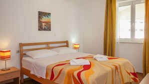 A neatly made bed with a colorful blanket, a bedside lamp, and a painting on the wall. - Apartment Elena by Interhome (Senj)