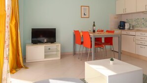 A living room with a TV, a dining table with red chairs, and a kitchen area with cabinets and a coffee maker. - Apartment Elena by Interhome (Senj)