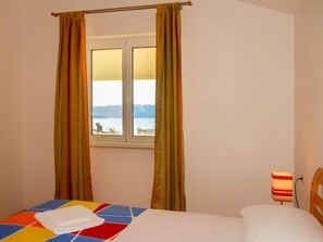 A hotel room with a bed, a window with curtains, a bedside table with a lamp, and a view of the sea. - Apartment Ivana by Interhome (Senj)