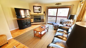A living room with a television, fireplace, sofa, and a view of the outdoors through a sliding door.