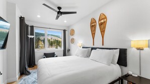 A modern hotel room with a large bed, a ceiling fan, a view of the outdoors, and a nightstand with a lamp.