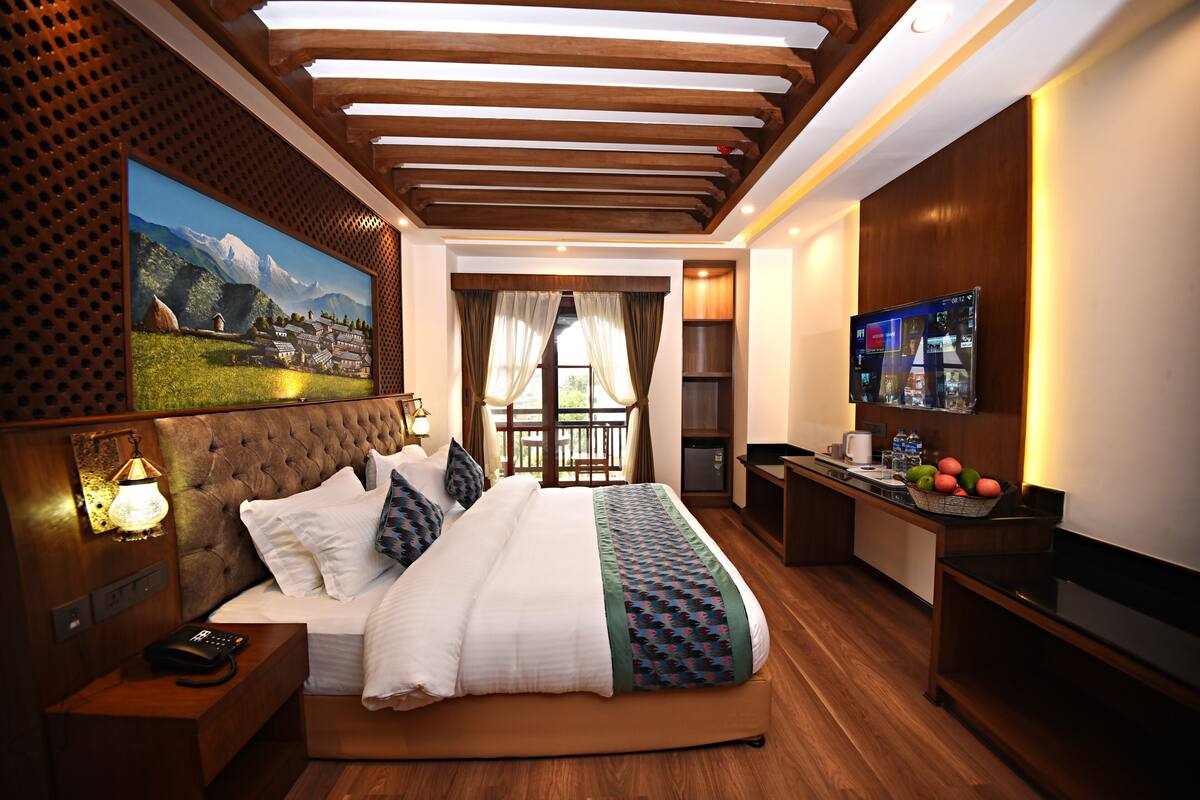 Une chambre d’hôtel avec un grand lit, une télévision, un bureau et un balcon offrant une vue sur les montagnes.