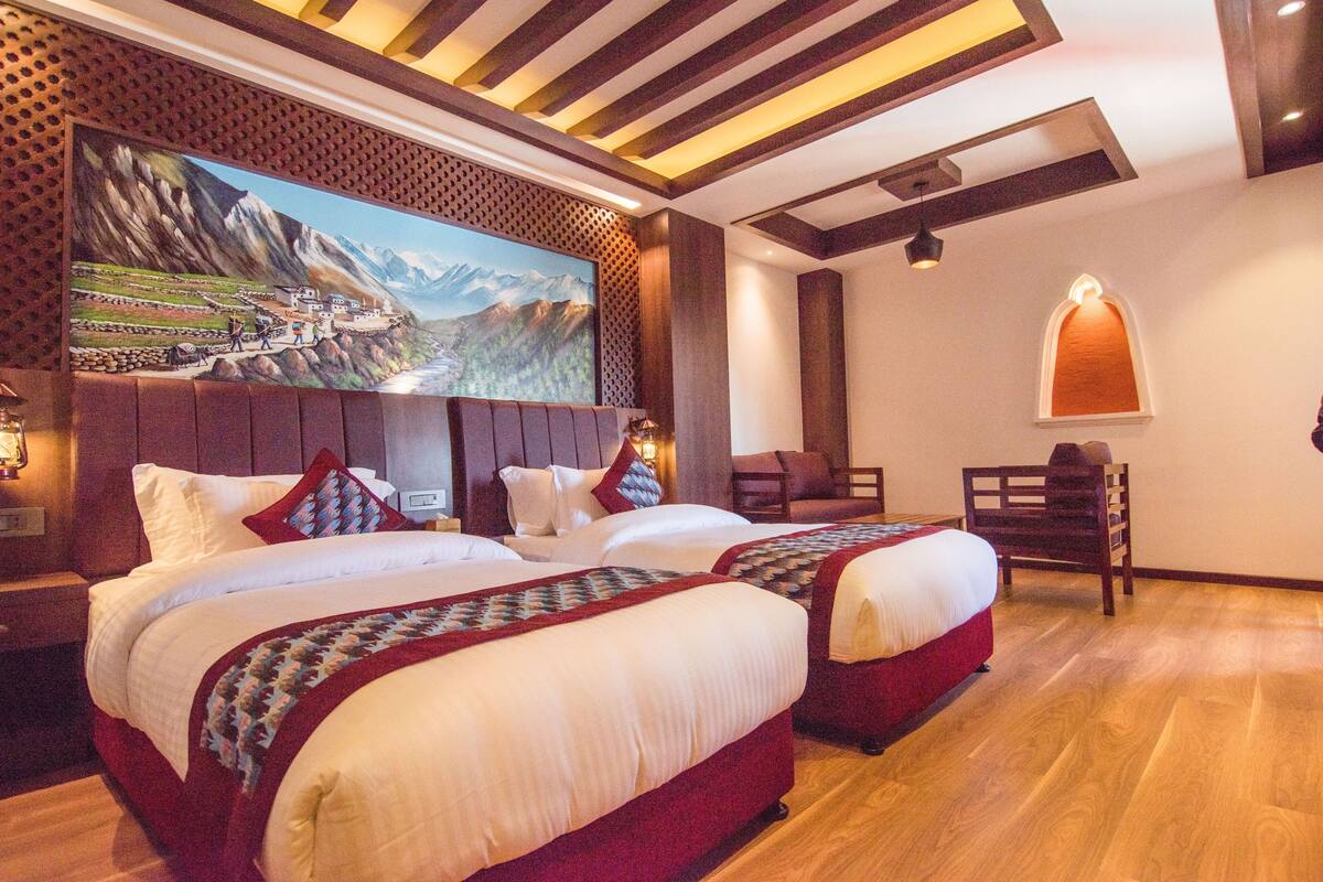 Une chambre d’hôtel avec deux lits, un plancher en bois, un grand tableau au mur et une chaise en bois.