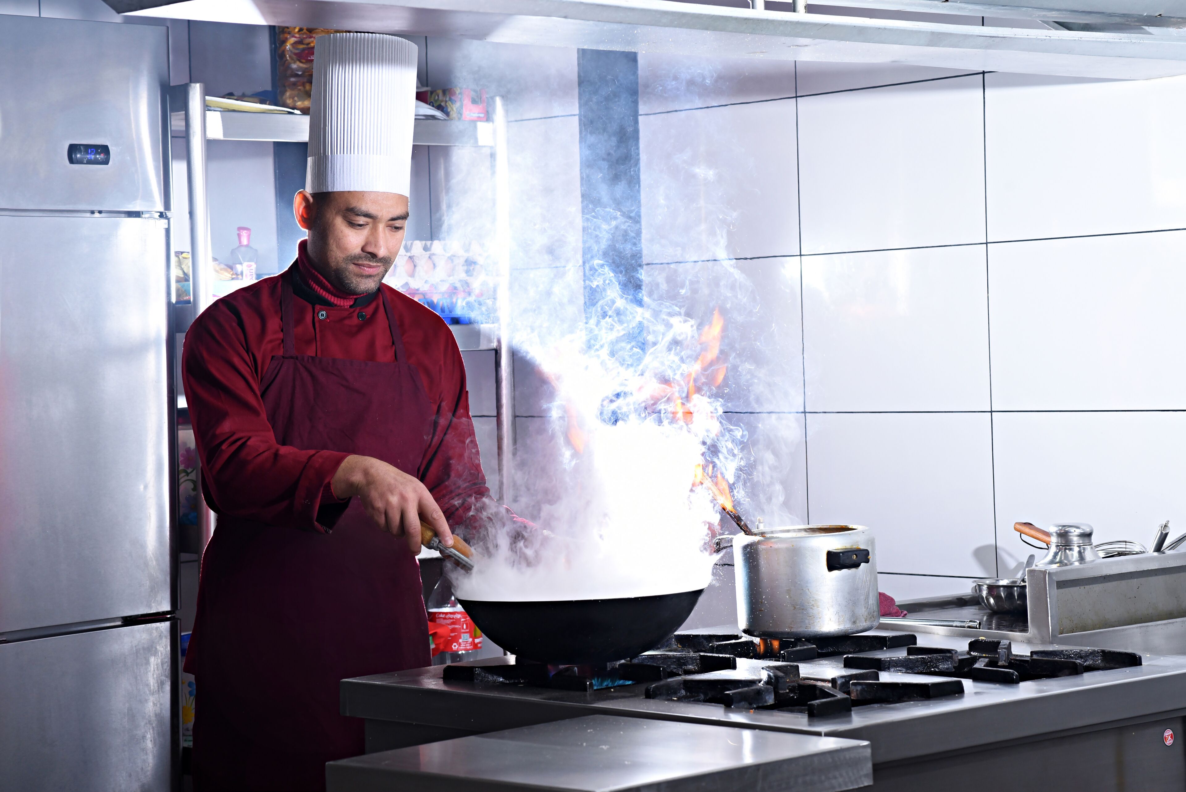 A chef in a red uniform cooking with a wok on a stove in a modern kitchen.