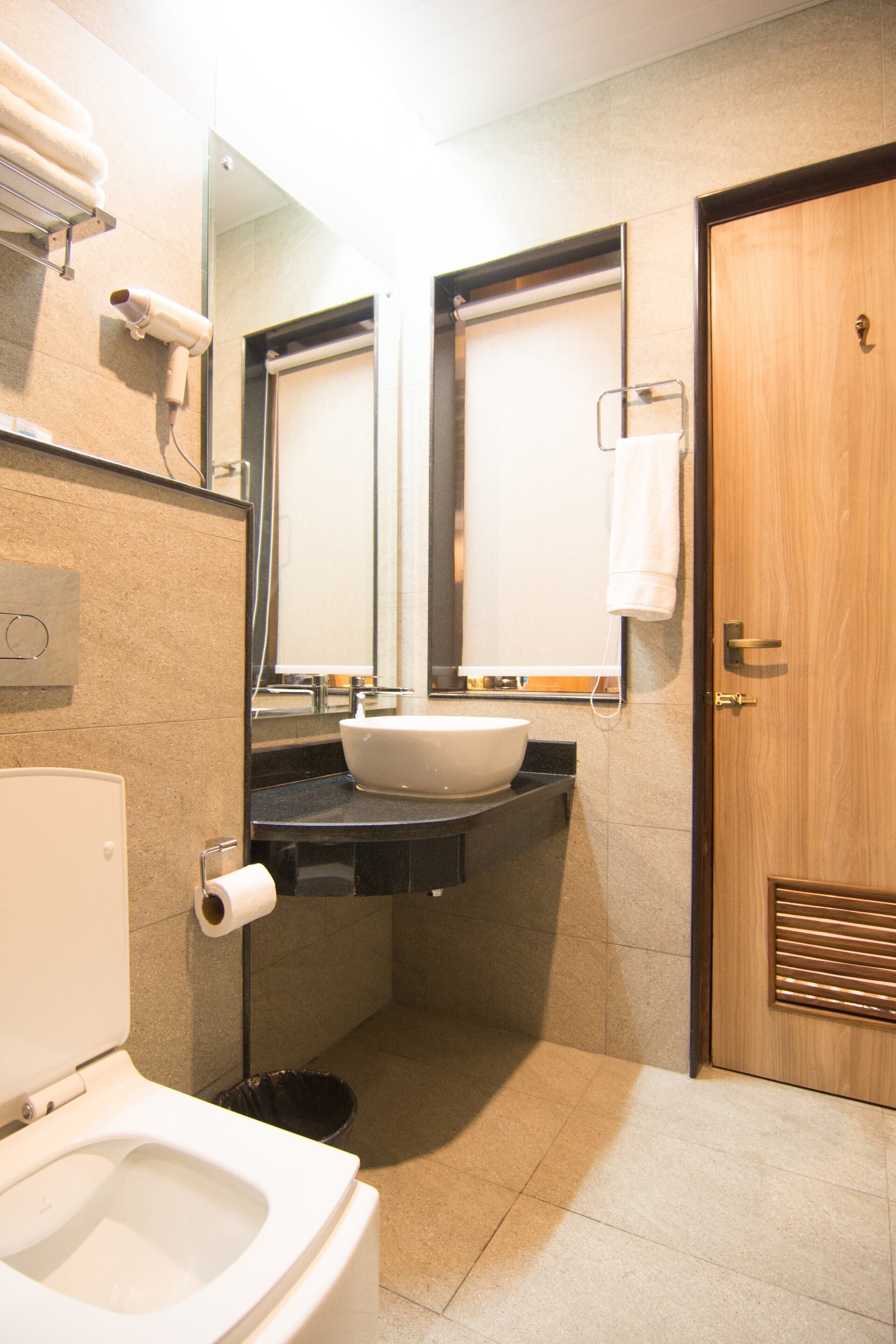 A compact bathroom with a white toilet, a sink with a mirror above it, a towel rack, and a wooden door.