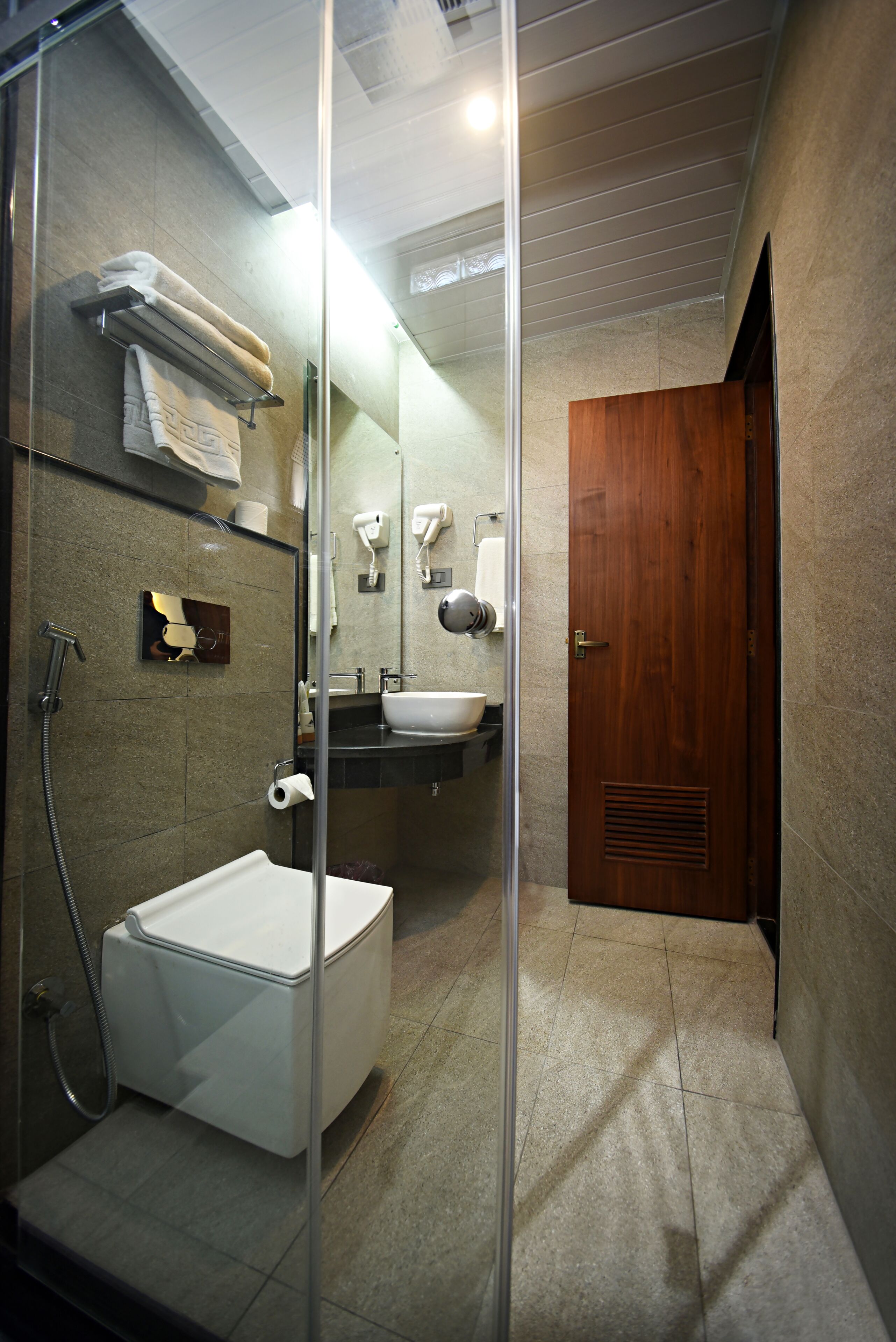 Ein modernes Badezimmer mit einer Glaskabine zur Dusche, einer weißen Badewanne, einem Waschbecken und einer Holztür.