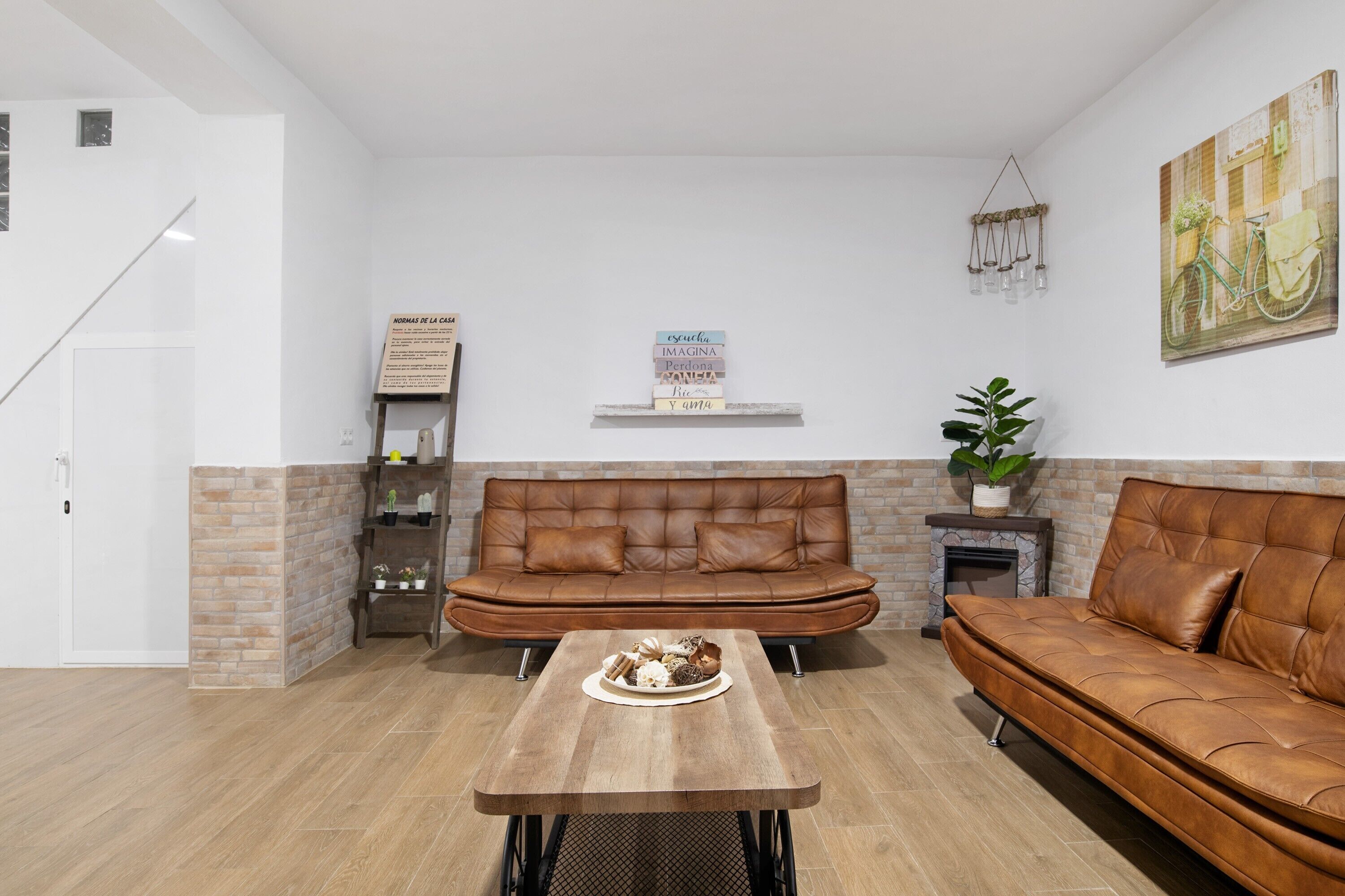 A living room with a brown leather sofa, a wooden coffee table, and a brick accent wall.