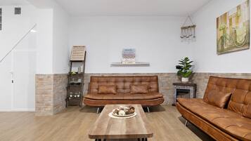 A living room with a brown leather sofa, a wooden coffee table, and a brick accent wall.