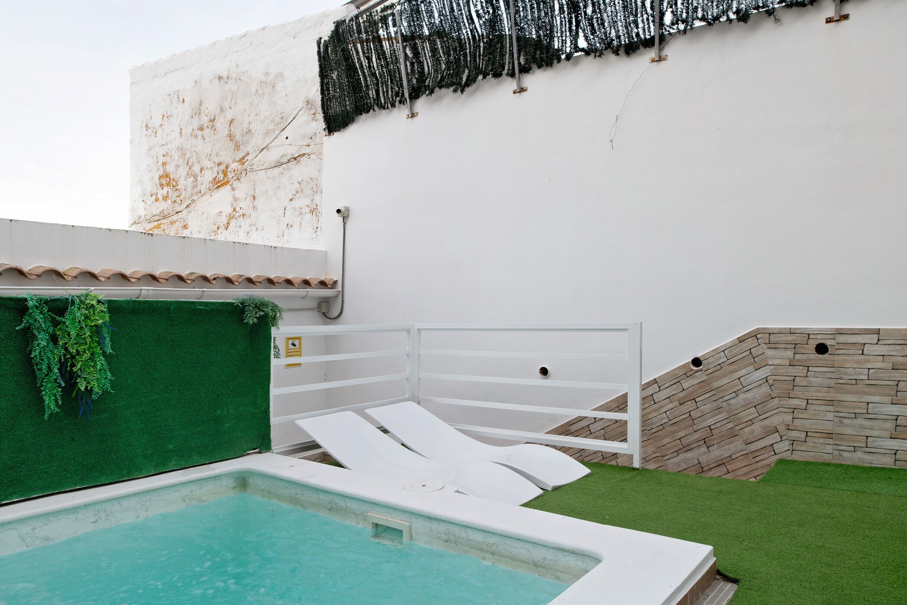 A swimming pool with white lounge chairs, a green wall with plants, and a stone wall.
