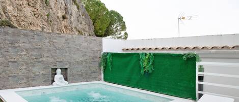 A spa area with a hot tub, white lounge chairs, a stone wall, and a green wall with plants.