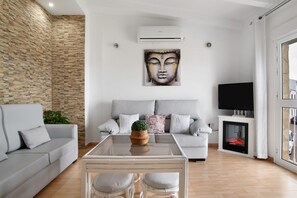 Una sala de estar con pared de piedra, un sofá, un televisor, una chimenea y un cuadro de Buda.