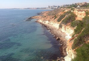 A coastal landscape with a rocky shoreline, clear blue sea, and a distant city skyline. - Villa with Private Pool, Terrace, A/C and Wi-Fi (San Miguel de Salinas)