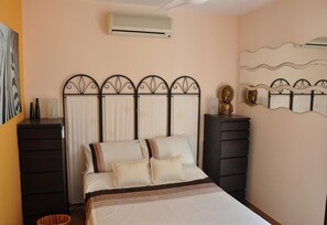 A bedroom with a bed, a dresser, an air conditioner, and a decorative head sculpture.